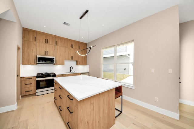 kitchen with gas range oven, stainless steel microwave, light wood-style floors, a kitchen island, and backsplash