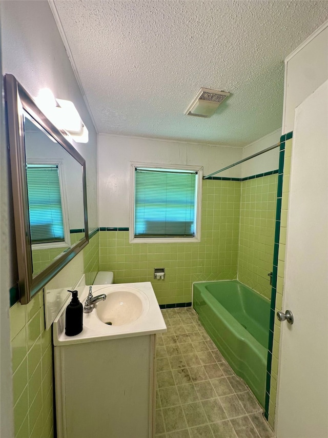 3605 Lawn Oak Dr, Orange, TX 77632 - bathroom with tile walls, a textured ceiling, vanity, a wainscoted wall, and washtub / shower combination