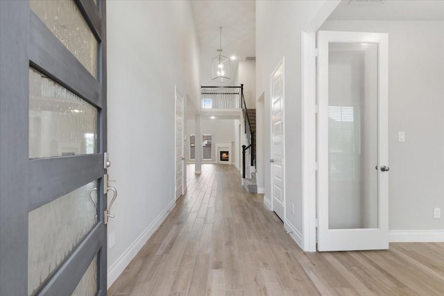 corridor featuring light wood finished floors, a high ceiling, and baseboards