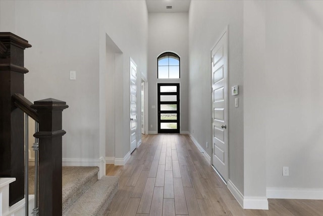 foyer entrance with a high ceiling, light wood finished floors, baseboards, and stairway