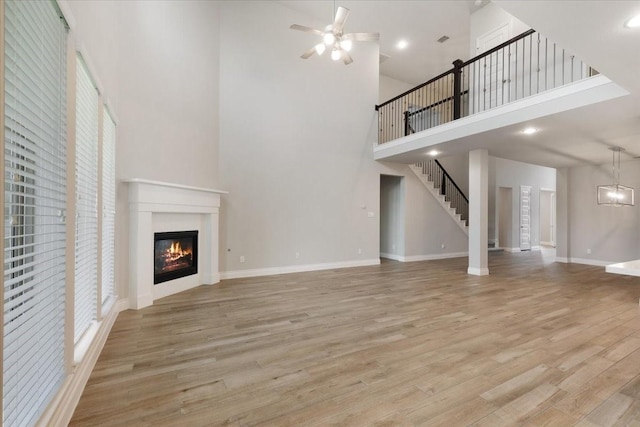 unfurnished living room featuring a towering ceiling, a glass covered fireplace, wood finished floors, a ceiling fan, and baseboards