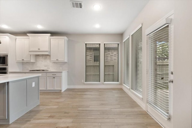 kitchen with appliances with stainless steel finishes, light countertops, white cabinets, under cabinet range hood, and light wood finished floors