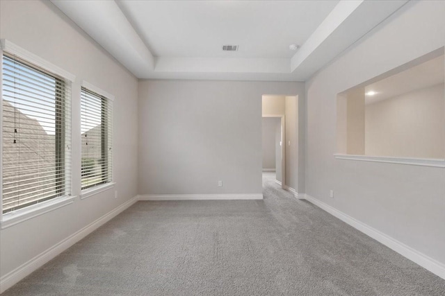 spare room with a raised ceiling, carpet, and baseboards