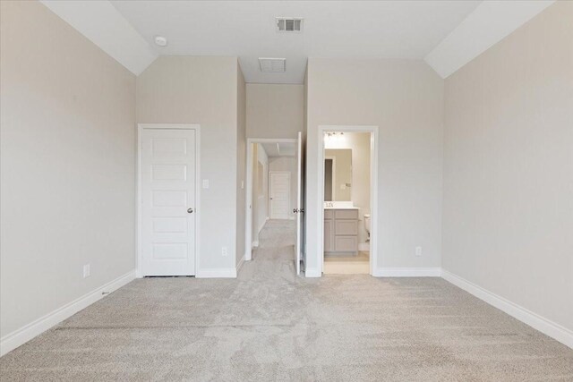 unfurnished bedroom with vaulted ceiling, light carpet, baseboards, and ensuite bathroom
