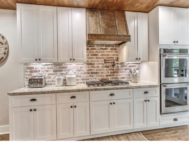 41103 Mill Creek Rd, Magnolia, TX 77354 - kitchen with appliances with stainless steel finishes, white cabinets, premium range hood, light stone counters, and wood ceiling