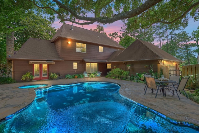 pool at dusk with french doors, a patio area, a pool with connected hot tub, and fence