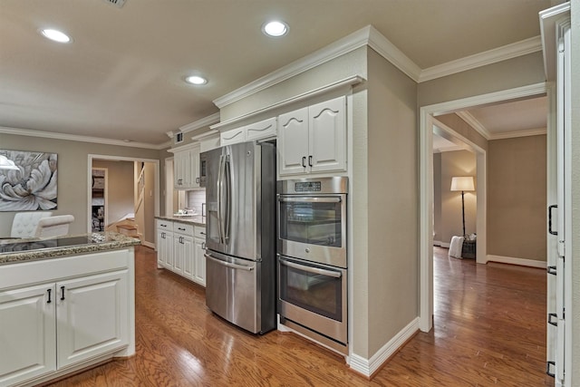 kitchen with appliances with stainless steel finishes, wood finished floors, white cabinets, ornamental molding, and recessed lighting