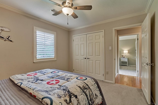 bedroom featuring light colored carpet, ornamental molding, a closet, a ceiling fan, and baseboards