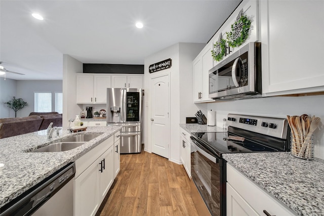 kitchen featuring appliances with stainless steel finishes, a sink, light wood-style floors, white cabinets, and recessed lighting