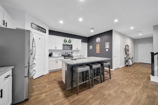 kitchen with stainless steel appliances, light wood finished floors, white cabinets, a center island with sink, and recessed lighting