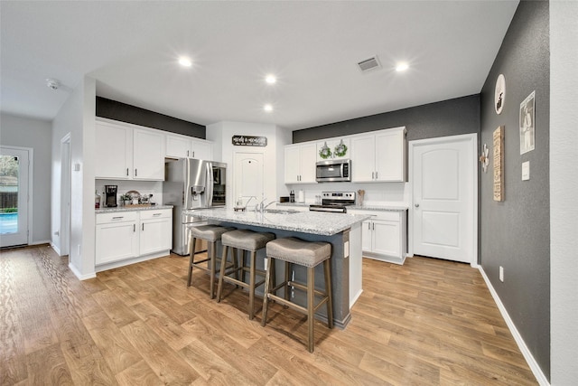 kitchen featuring stainless steel appliances, a breakfast bar area, light wood-style floors, white cabinets, and recessed lighting
