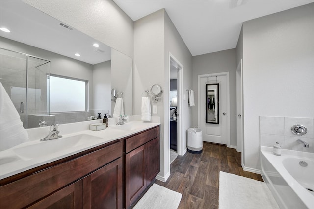 full bath featuring a stall shower, a garden tub, wood finished floors, a walk in closet, and baseboards