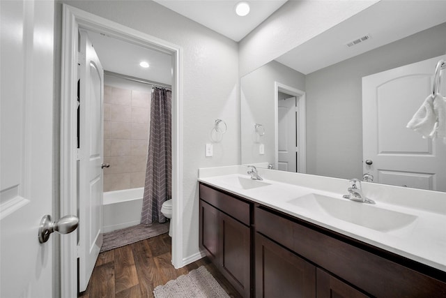bathroom featuring wood finished floors, toilet, double vanity, shower / bathtub combination with curtain, and recessed lighting
