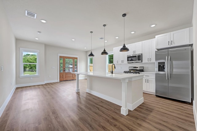 206 S 4th St, Conroe, TX 77301 - kitchen with appliances with stainless steel finishes, wood finished floors, a kitchen island with sink, tasteful backsplash, and baseboards