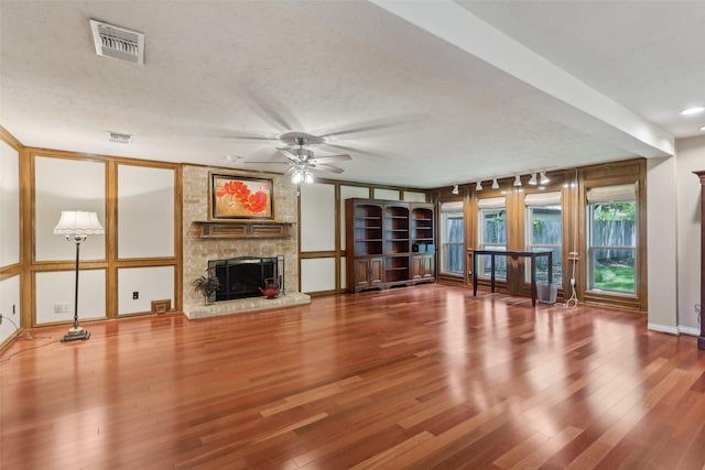 unfurnished living room with ceiling fan, a stone fireplace, wood finished floors, and a textured ceiling