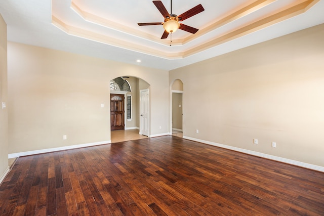 empty room featuring arched walkways, a raised ceiling, a ceiling fan, wood finished floors, and recessed lighting