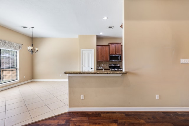 kitchen with appliances with stainless steel finishes, stone countertops, a chandelier, decorative backsplash, and pendant lighting