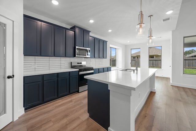 21705 Southern Valley Ln, New Caney, TX 77357 - kitchen with stainless steel appliances, light countertops, a center island with sink, light wood-type flooring, and decorative backsplash