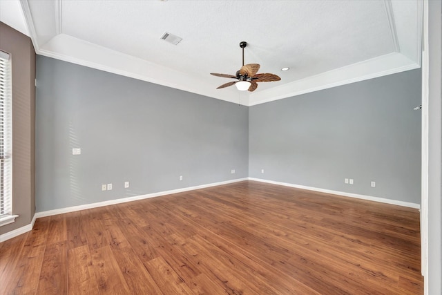 spare room with ceiling fan, ornamental molding, baseboards, wood finished floors, and a raised ceiling