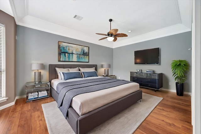 bedroom featuring a raised ceiling, baseboards, wood finished floors, ornamental molding, and a ceiling fan