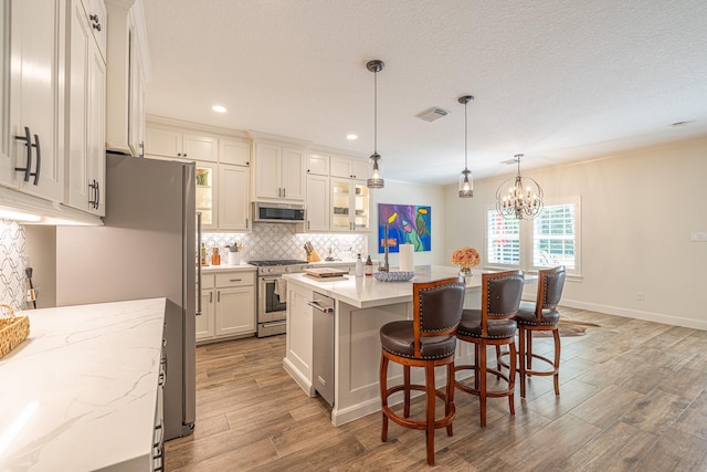 kitchen featuring stainless steel appliances, backsplash, wood finished floors, a chandelier, and a kitchen island