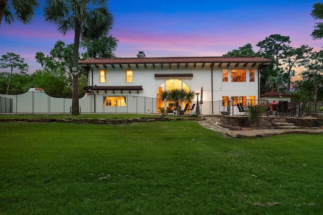 back of property at dusk with a tile roof, stucco siding, and a chimney