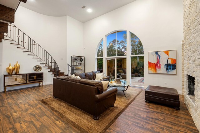 living area featuring a high ceiling, wood finished floors, stairway, a stone fireplace, and baseboards