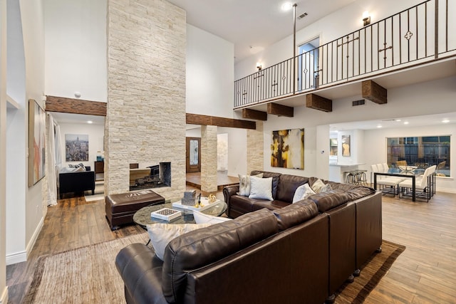 living room featuring a high ceiling, hardwood / wood-style floors, a stone fireplace, and baseboards