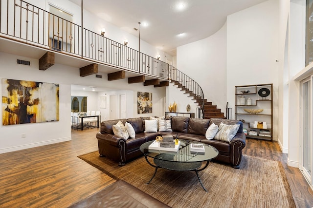 living area with a towering ceiling, wood finished floors, baseboards, and stairs