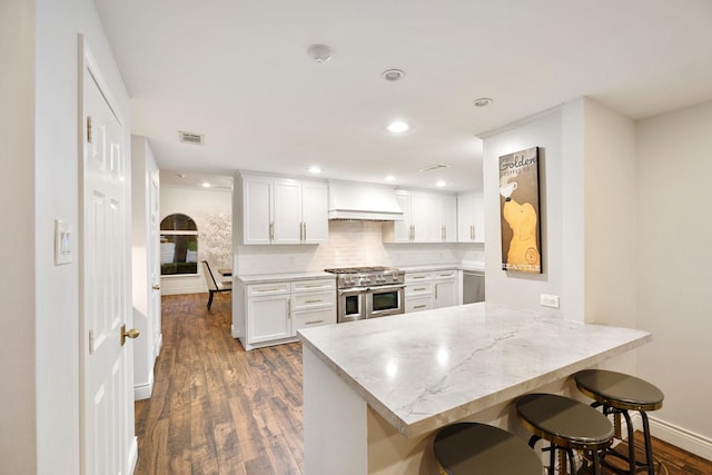 kitchen featuring range with two ovens, dark wood-style flooring, a breakfast bar, premium range hood, and white cabinetry