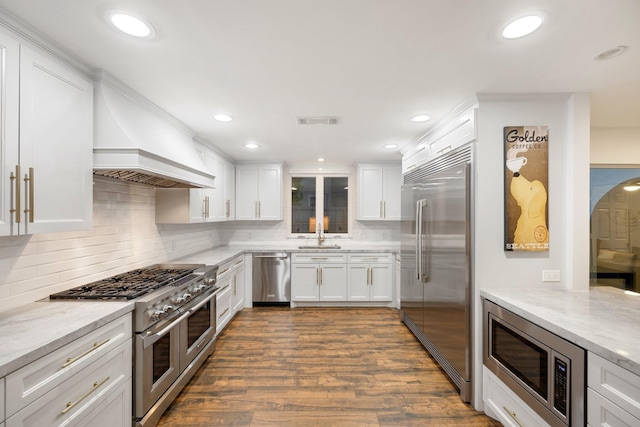 kitchen with built in appliances, white cabinets, light stone countertops, dark wood-style flooring, and tasteful backsplash