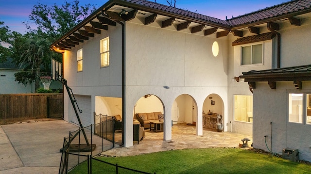 rear view of house featuring stucco siding, concrete driveway, a garage, an outdoor hangout area, and a patio