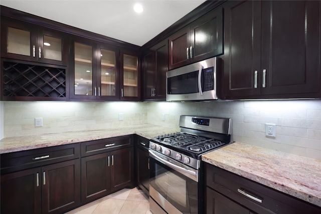 5418 Poinciana Dr, Houston, TX 77092 - kitchen featuring appliances with stainless steel finishes, light stone countertops, decorative backsplash, glass insert cabinets, and light tile patterned flooring