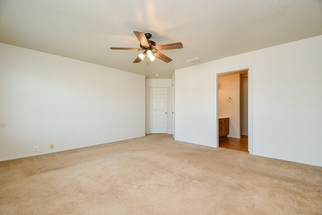 unfurnished bedroom with light colored carpet, ensuite bath, baseboards, and ceiling fan