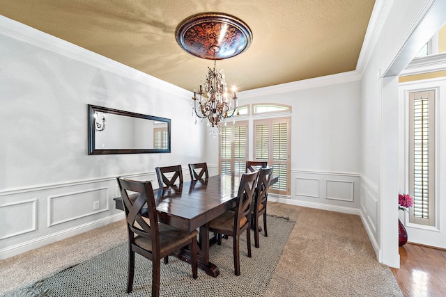 carpeted dining space featuring a decorative wall, a chandelier, crown molding, a wainscoted wall, and a textured ceiling