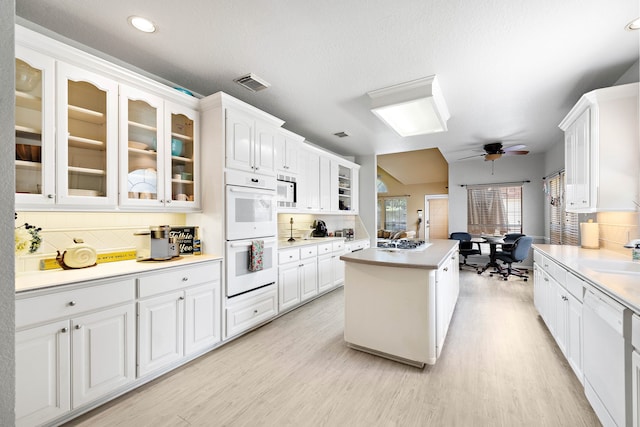 kitchen with white appliances, a center island, a ceiling fan, tasteful backsplash, and glass insert cabinets
