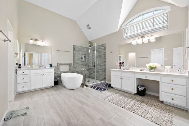 bathroom with high vaulted ceiling, a stall shower, a freestanding bath, and two vanities