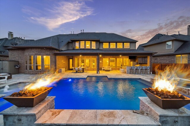 2011 Greenvine Cir, Katy, TX 77494 - back of property at dusk featuring a fire pit, a patio area, an outdoor pool, brick siding, and roof with shingles