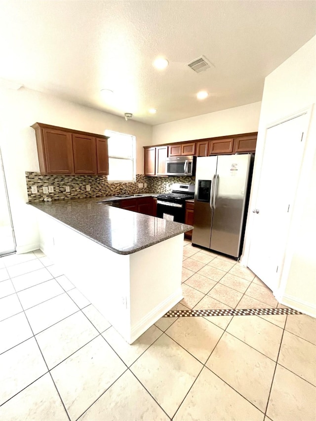 13150 Lawsons Creek Ln, Houston, TX 77072 - kitchen with stainless steel appliances, a peninsula, tasteful backsplash, light tile patterned flooring, and dark stone counters