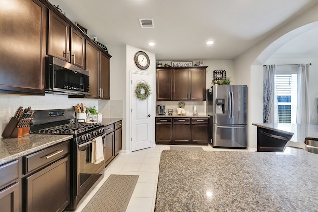 8619 Morning Dove Ln, Baytown, TX 77521 - kitchen featuring appliances with stainless steel finishes, arched walkways, dark brown cabinets, tasteful backsplash, and light stone countertops