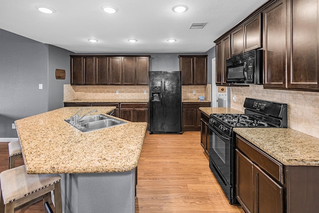 kitchen featuring black appliances, a sink, light wood-style flooring, dark brown cabinets, and a breakfast bar area