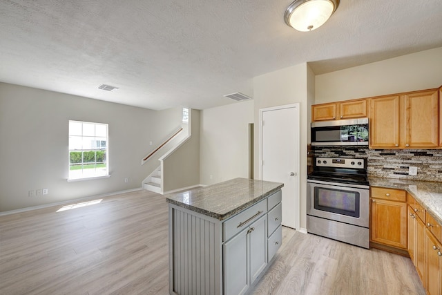 2802 Austin St, Houston, TX 77004 - kitchen featuring appliances with stainless steel finishes, light wood-style floors, open floor plan, tasteful backsplash, and a center island