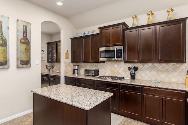 18107 Banpo Ct, Houston, TX 77044 - kitchen with stainless steel appliances, arched walkways, decorative backsplash, light stone counters, and a kitchen island