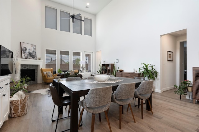 7507 Zion Grove Ct, Katy, TX 77493 - dining room with light wood-type flooring, a ceiling fan, a fireplace, a towering ceiling, and baseboards