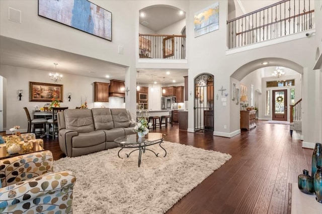 living room with a chandelier, dark wood-style flooring, arched walkways, and a high ceiling