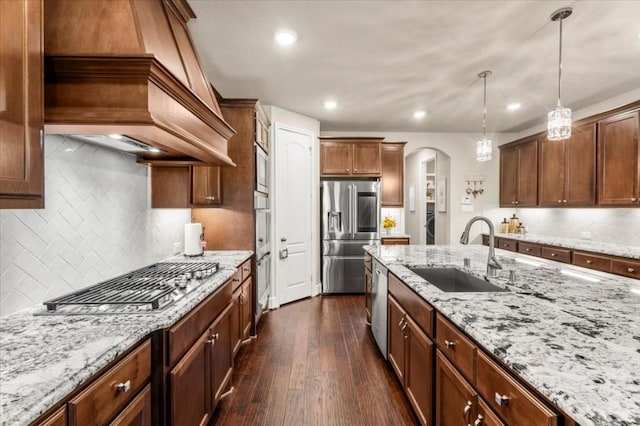 kitchen with appliances with stainless steel finishes, a sink, arched walkways, dark wood finished floors, and hanging light fixtures