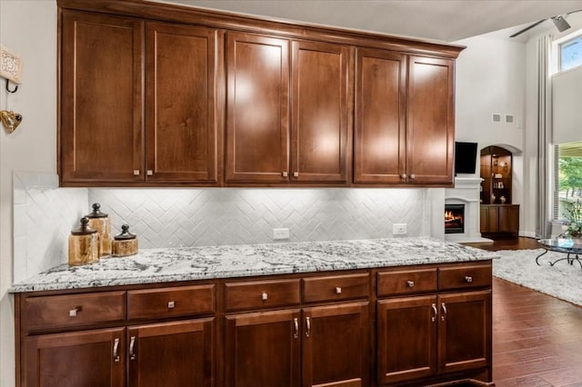 kitchen featuring dark wood-type flooring, light stone countertops, decorative backsplash, and a lit fireplace
