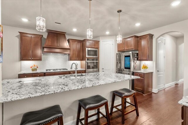 kitchen featuring appliances with stainless steel finishes, premium range hood, a sink, arched walkways, and backsplash