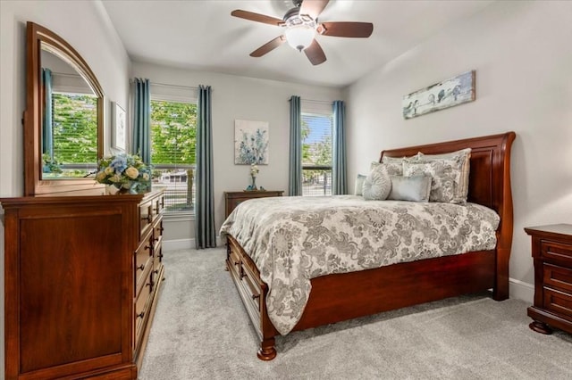 bedroom featuring multiple windows, light carpet, a ceiling fan, and baseboards