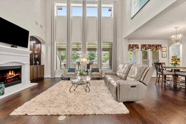 living area with a towering ceiling, healthy amount of natural light, dark wood-type flooring, arched walkways, and a lit fireplace